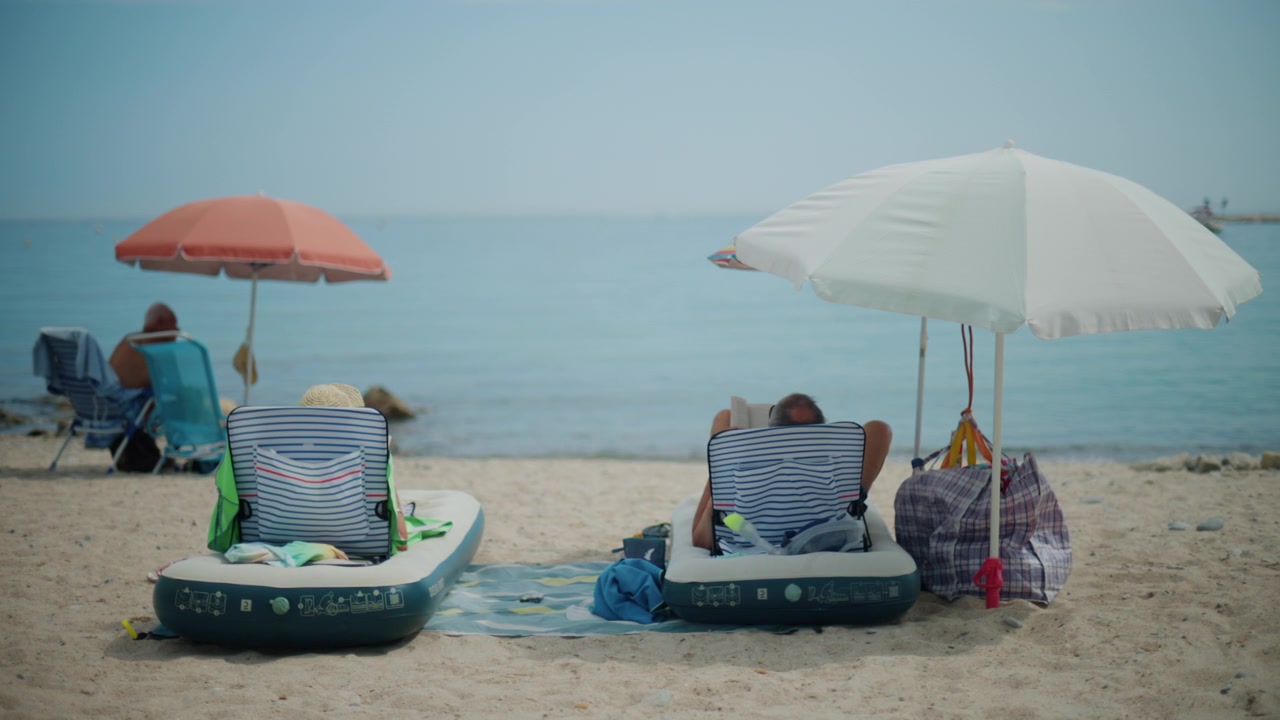 Persone che si godono il tempo libero su una spiaggia sabbiosa, sedute su lettini gonfiabili e sedie da spiaggia tradizionali sotto gli ombrelloni.
