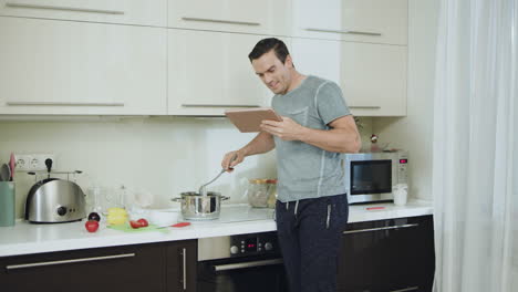 hombre feliz cocinando una cena saludable en la cocina de su casa con una tableta.