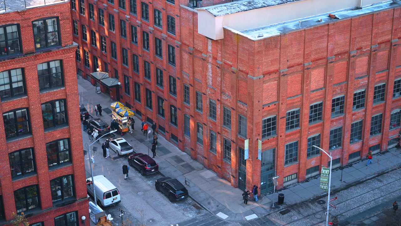 New York, USA, 1. juli 2026: Røde mursteinslagerbygninger i en gate i DUMBO. Et hevet perspektiv viser fotgjengere, parkerte kjøretøy og en salgsvogn mellom røde mursteinslagerbygninger.