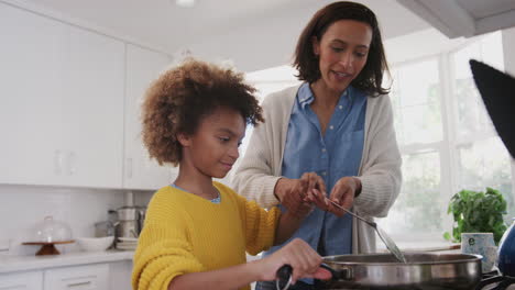mother helping her pre-teen daughter cook food in a pan at the hob in the kitchen,close up
