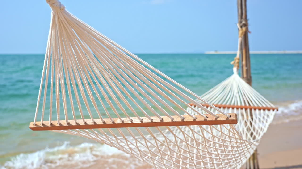 toma estática de una hamaca vacía que se mueve lentamente por el viento con olas tranquilas que llegan a la orilla desde el océano