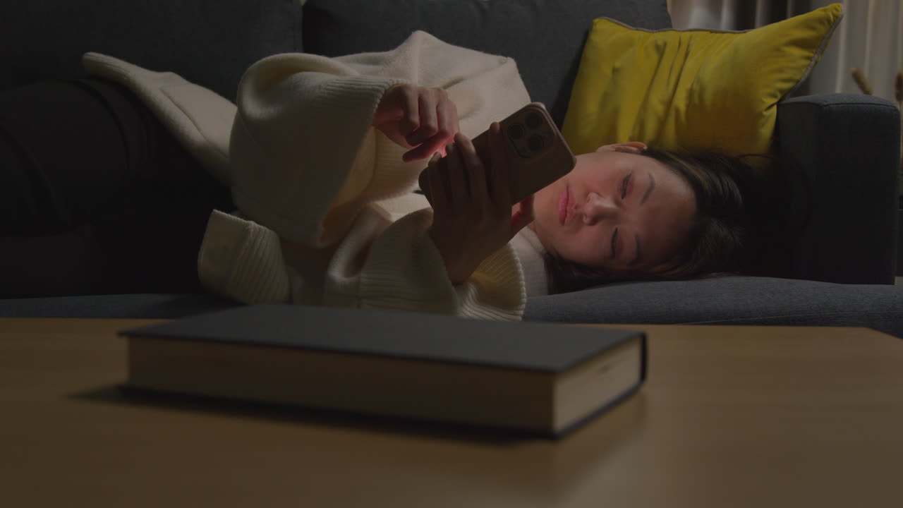 집에서 저녁을 보내고 소파에 누워 휴대전화를 들고 인터넷이나 소셜 미디어를 스크롤하는 여성 8