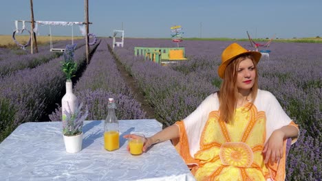 woman in hippie style enjoying the day with orange juice on table in lavender field, reflecting on life