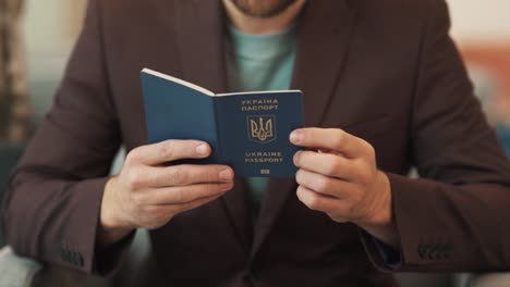 primer plano de las manos de un hombre tomando un pasaporte ucraniano y mirándolo contra el fondo de la chaqueta de un hombre