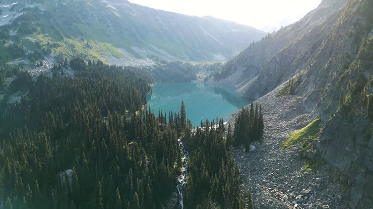 Volando verso il lago turchese sopra il ruscello nella foresta con il sole del mattino sullo sfondo