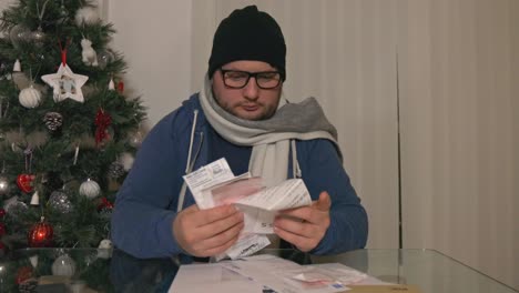 stressed man sitting at the desk, looking at bills to pay one by one