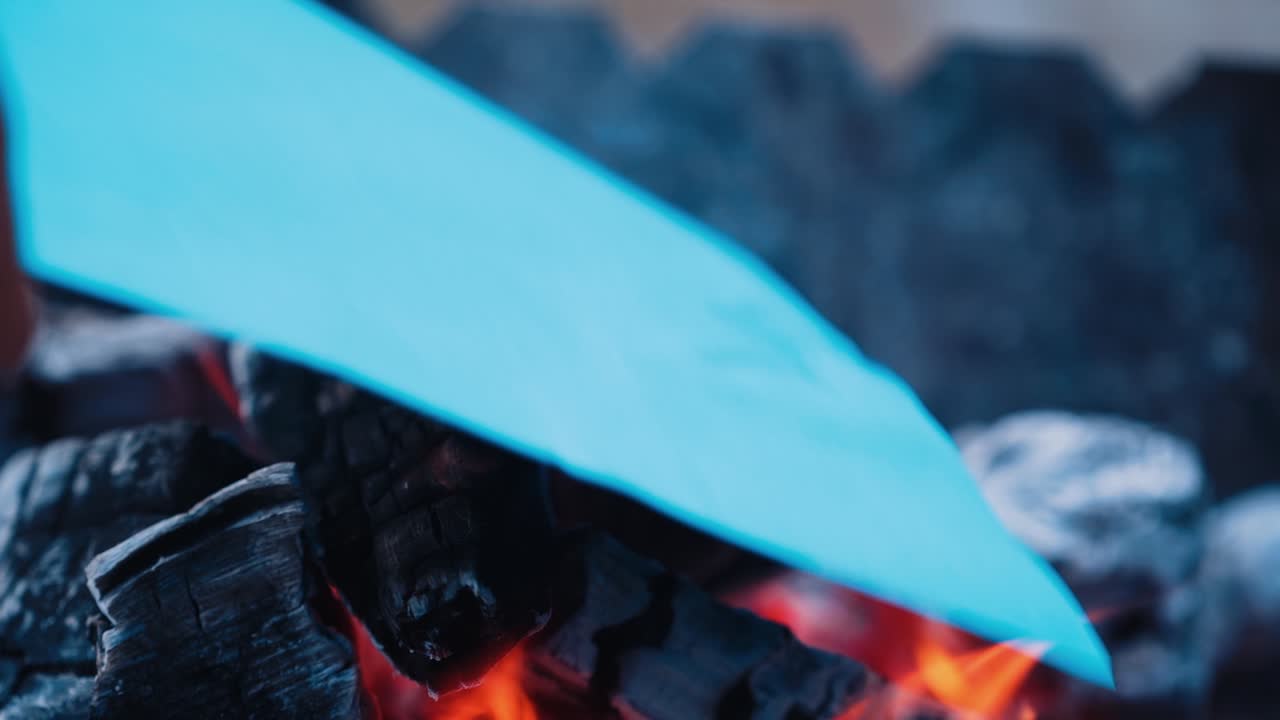 Black charcoal in bonfire close-up. White paper list falling into the fire and burning brightly. Slow motion.