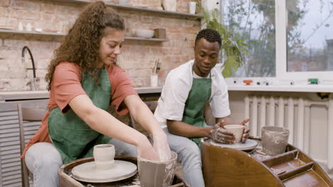 employees wearing green apron modeling ceramic pieces on potter wheel in a workshop while talking to each other 2