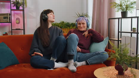 lesbian women family couple in wireless headphones dancing disco listening music song on home couch