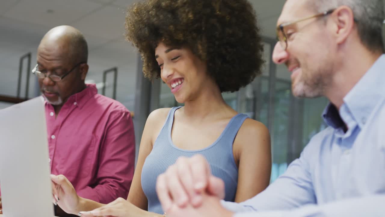Diverse male and female business colleagues smiling and using laptop