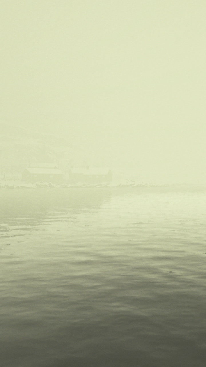 Cloudy fog covers landscape with buildings near water in winter season
