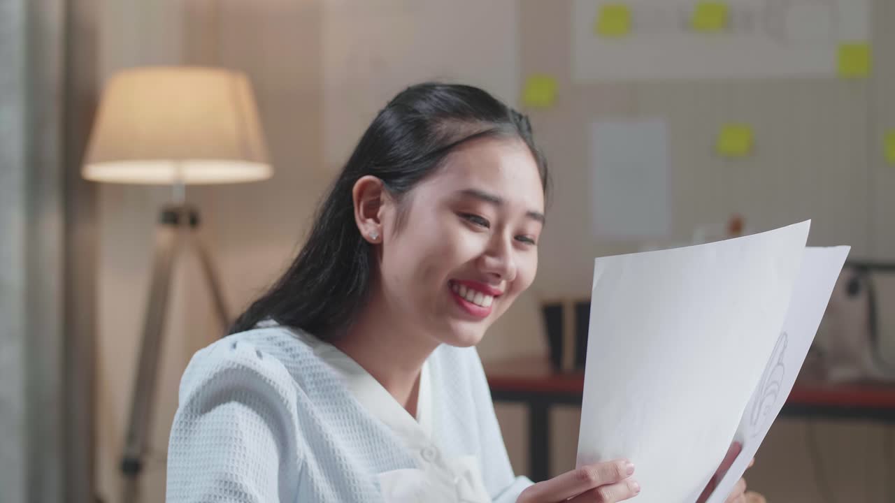 아시아 여성 디자이너의 클로즈업은 사무실에서 레이아웃을 보면서 머리를 긍정적으로 흔들고 있습니다.