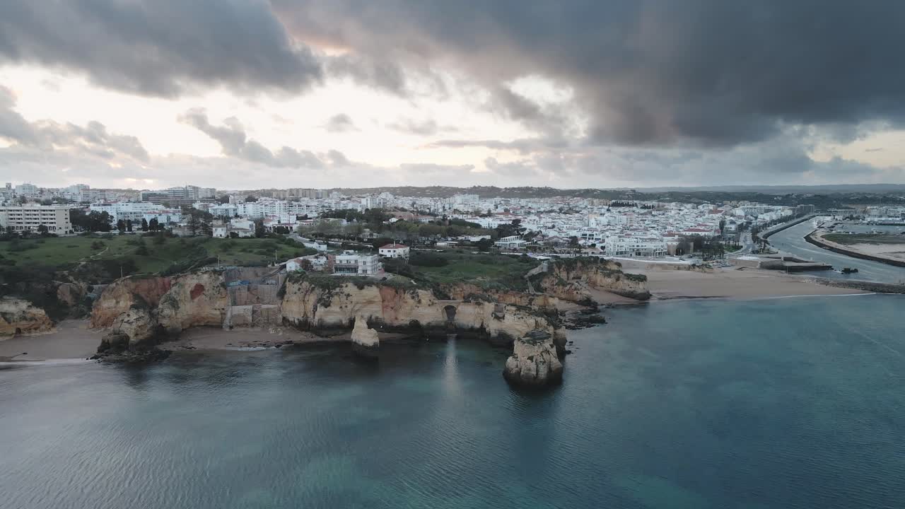 Aerial drone pulls back from close limestone formations revealing panoramic view of Lagos city and dramatic coastline