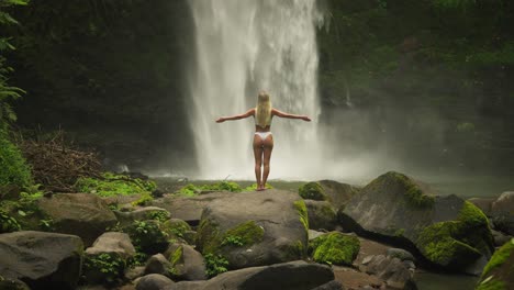 woman in white bikini raising arms greeting powerful stream of waterfall, nungnung