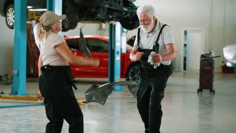 positive mechanic adult man and woman in uniform dancing in repair shop.