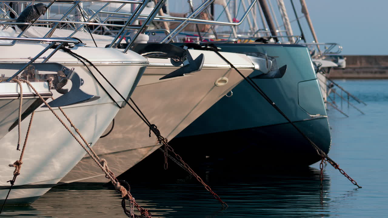 Side view of several luxury yachts moored side by side with ropes and anchors visible