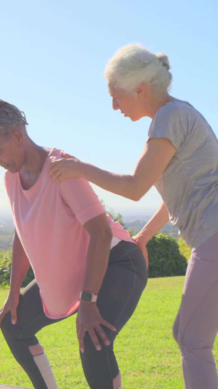 Vertical video: Stepping from right guide touching pink-top woman squatting at deck fixing form