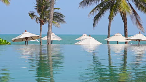 Leerer-Infinity-Pool-Und-Weiße-Sonnenschirme-Am-Strand