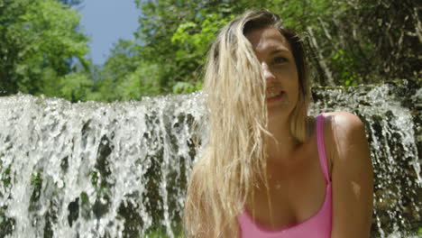 linda y divertida mujer joven sonríe y posa frente a una cascada en un entorno natural forestal