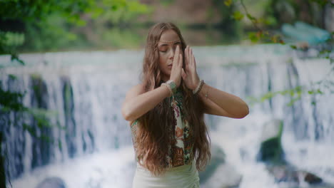 beautiful woman meditating in front of waterfall