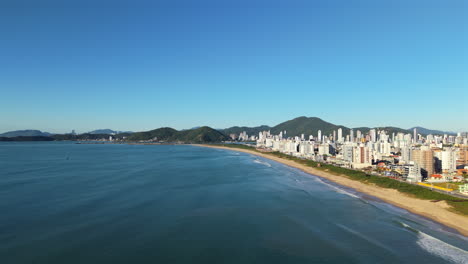 High drone shot over Navegantes’ ocean, city, and hills under bright sun