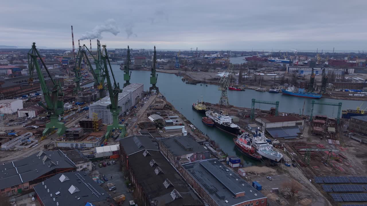 Aerial of Gdansk Shipyard industrial setting, Poland, cranes, ships, and Gdansk Harbour stretching into the distance with smoke rising
