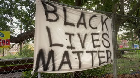 a sheet with the words black lives matter spray painted in black and hung on a chain link fence