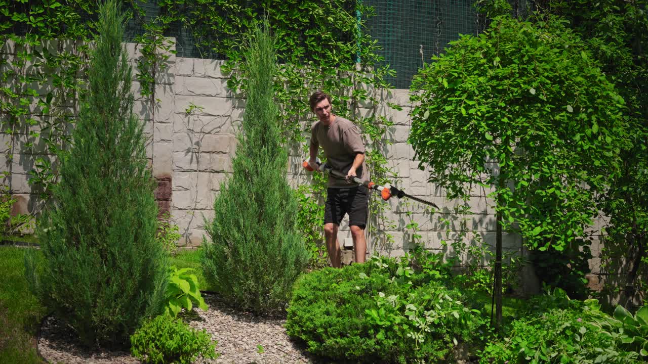 Man Trimming Bushes with a Long-Reach Hedge Trimmer in a Garden