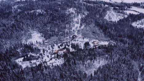 Luftdrohnenschuss,-Der-Rückwärts-Und-Weg-Vom-Holzfällerlager-In-Schneebedeckten,-Reifen-Kiefernwäldern-In-Den-Nördlichen-Gebieten-Fliegt,-Vor-Sonnenaufgang,-Blaue-Stunde,-Morgendämmerung