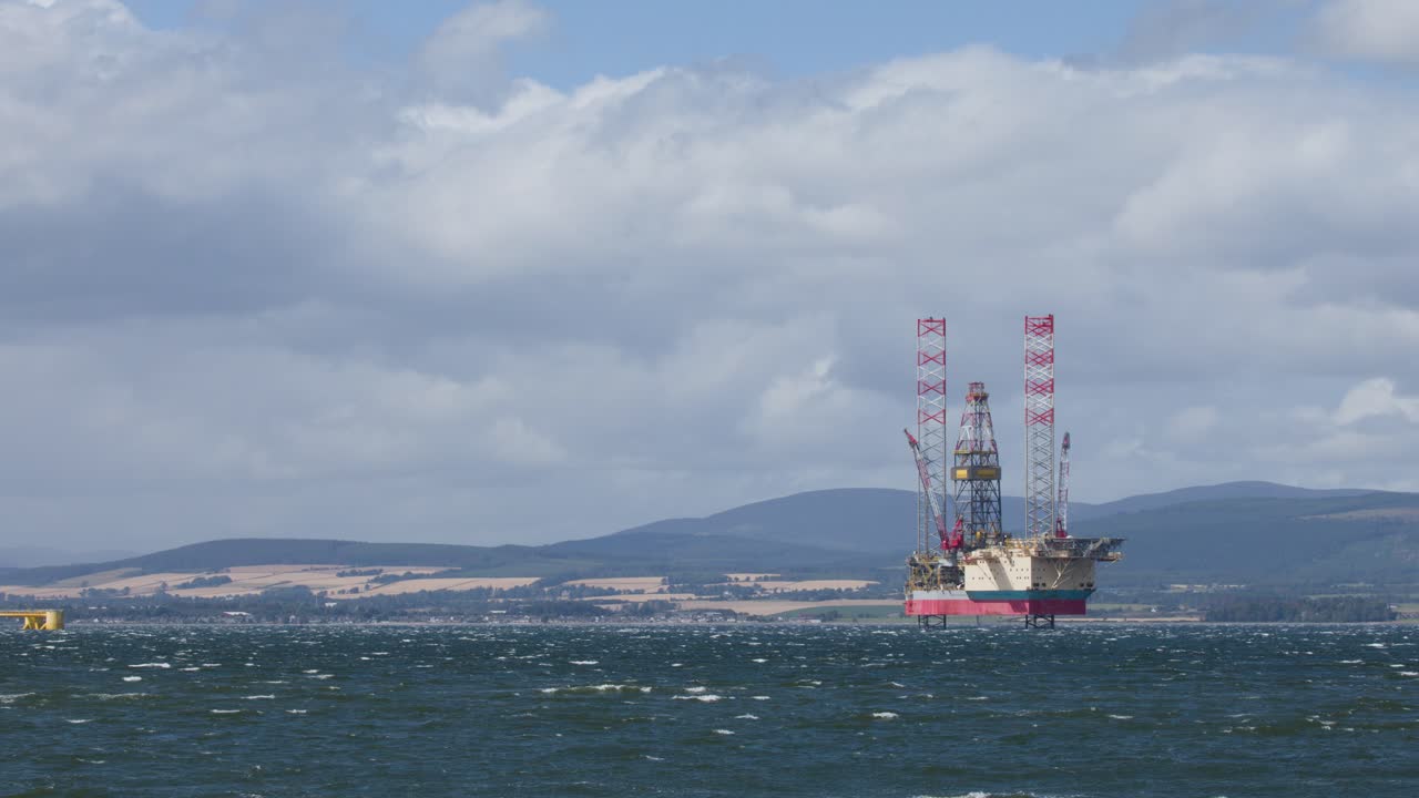 Offshore oil platform stands in windy Cromarty Firth, Scotland, with waves, hills, and moving clouds