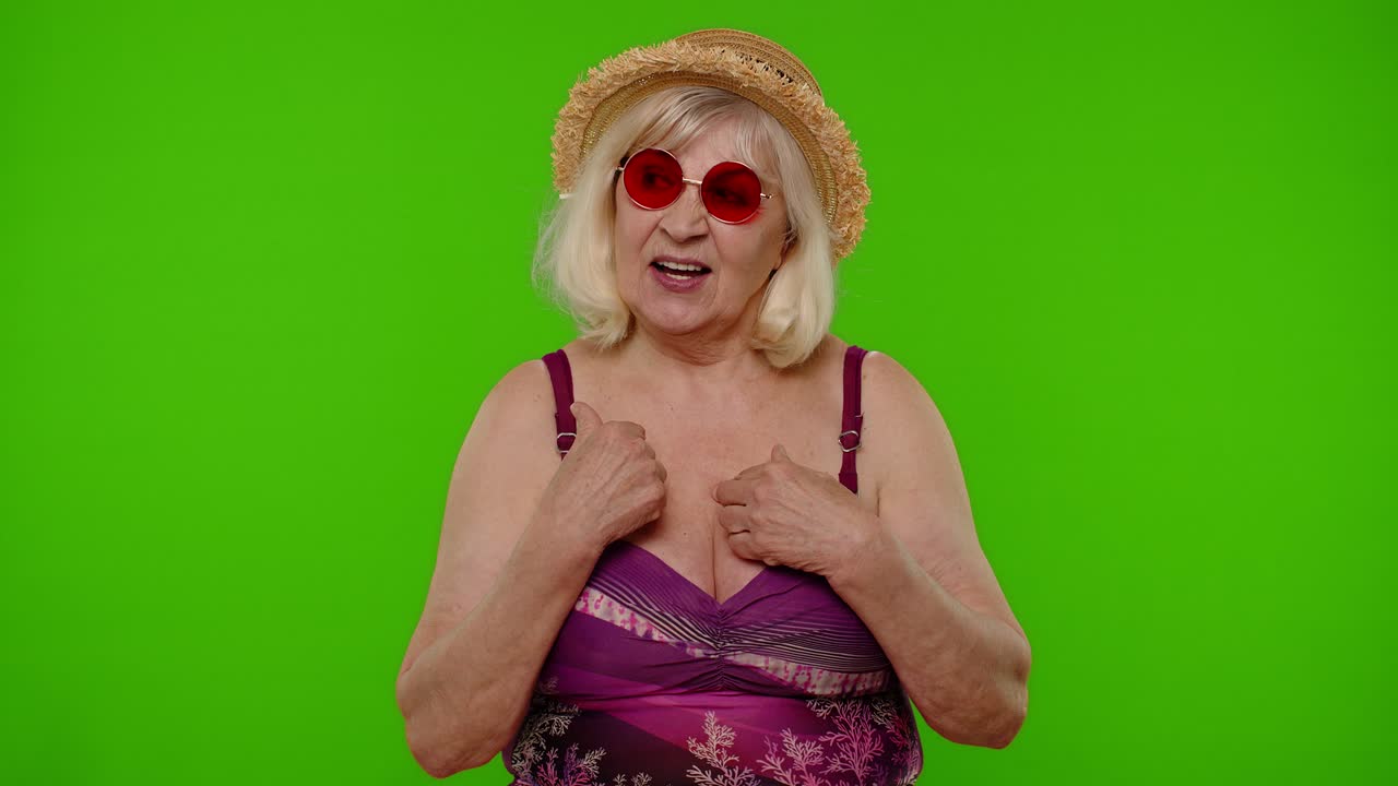 mujer madura viajera señalándose a sí misma, sonriendo satisfecha, satisfecha de su propia belleza y logros