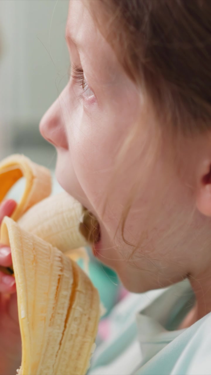 Primo piano di una bambina che mangia con illuminazione soffusa e espressione calma. La scena mostra il profilo laterale mentre la bambina interagisce con il suo pasto circondata da oggetti pastello colorati in un ambiente interno