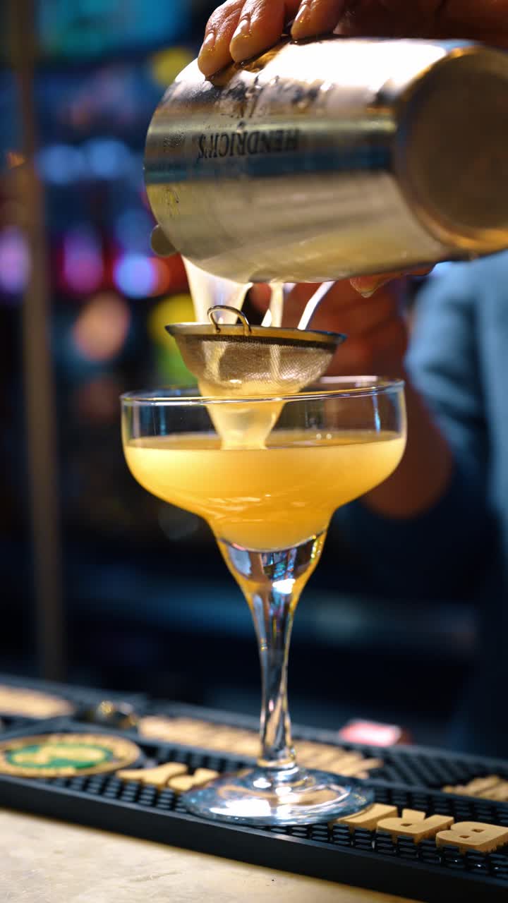 Barman che filtra un cocktail fresco attraverso un setaccio nel bicchiere. Primo piano delle mani che versano il liquido da uno shaker attraverso un colino professionale in un bicchiere coupe