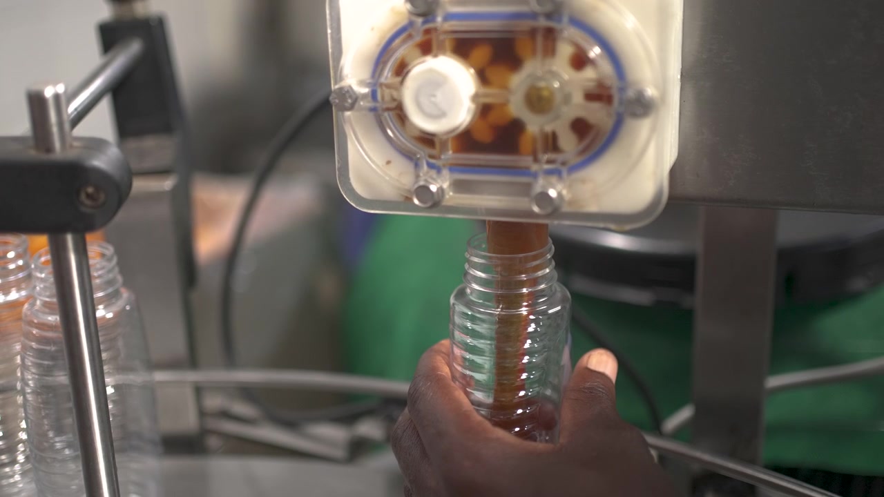 A worker operates a honey bottling machine, filling clear bottles with honey. Ideal for illustrating food production processes or industrial settings.
