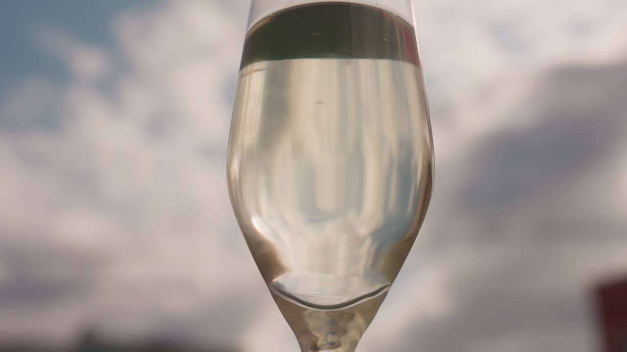 Primo piano di un flute di champagne su un cielo nuvoloso, eleganti bollicine e condensa catturano la luce dorata sopra il bokeh sfocato della città, atmosfera di festa intima su un tetto, toni caldi e tenui, messa a fuoco selettiva sul cristallo