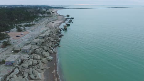 establishing aerial view of abandoned seaside fortification buildings at karosta northern forts on the beach of baltic sea , waves splash, overcast day, wide drone shot moving forward