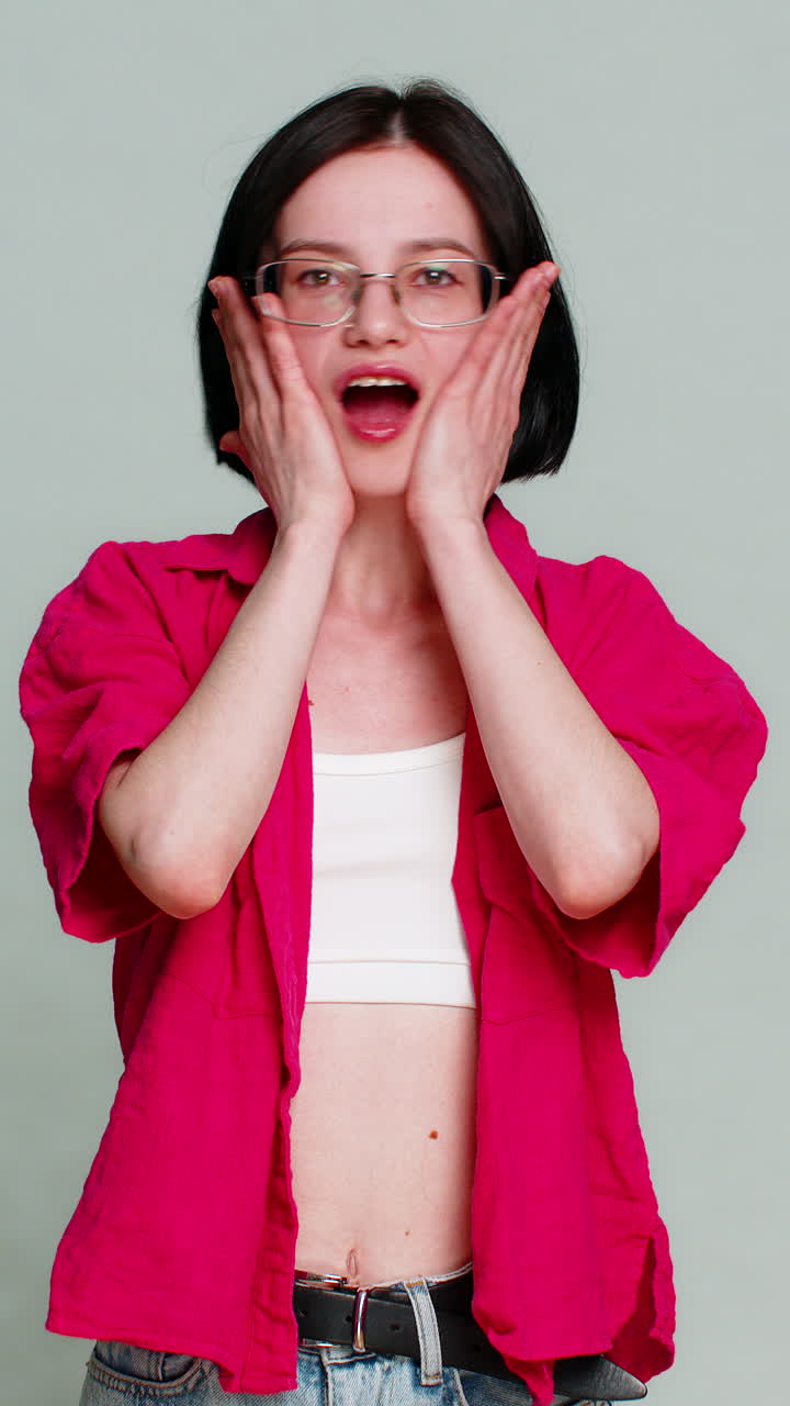 Young woman shocked screaming with open mouth holding cheeks reacting to unbelievable surprise news