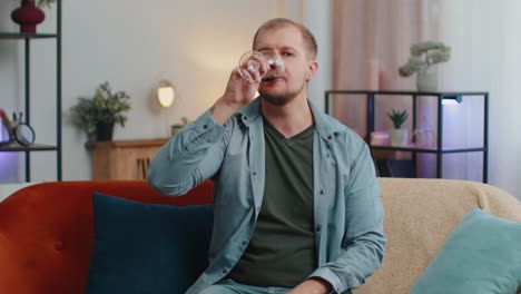 joven adulto feliz bebiendo un vaso de vino rojo celebrando el aniversario de cumpleaños ganando la lotería en casa