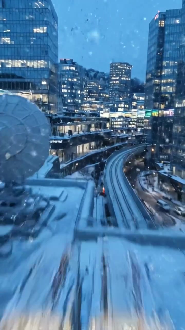 A Winter Cityscape at Dusk: Glowing Buildings, Snowflakes, and a Twisting Rail Track Create a Magical Urban Scene in the Heart of the City