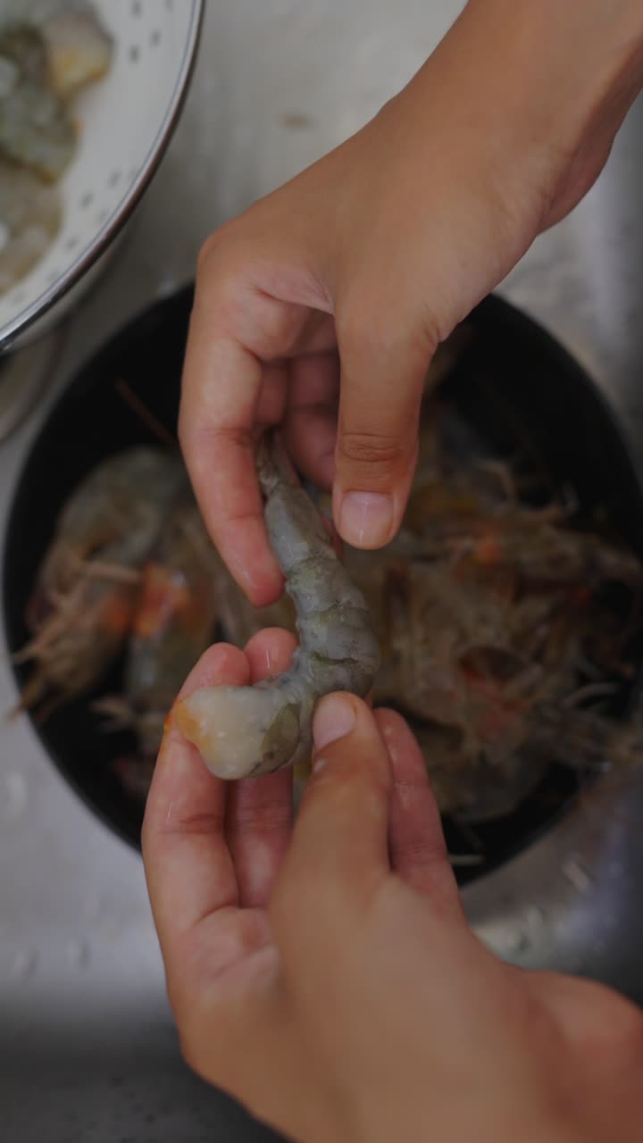 Hands peeling and cleaning raw shrimp for cooking.