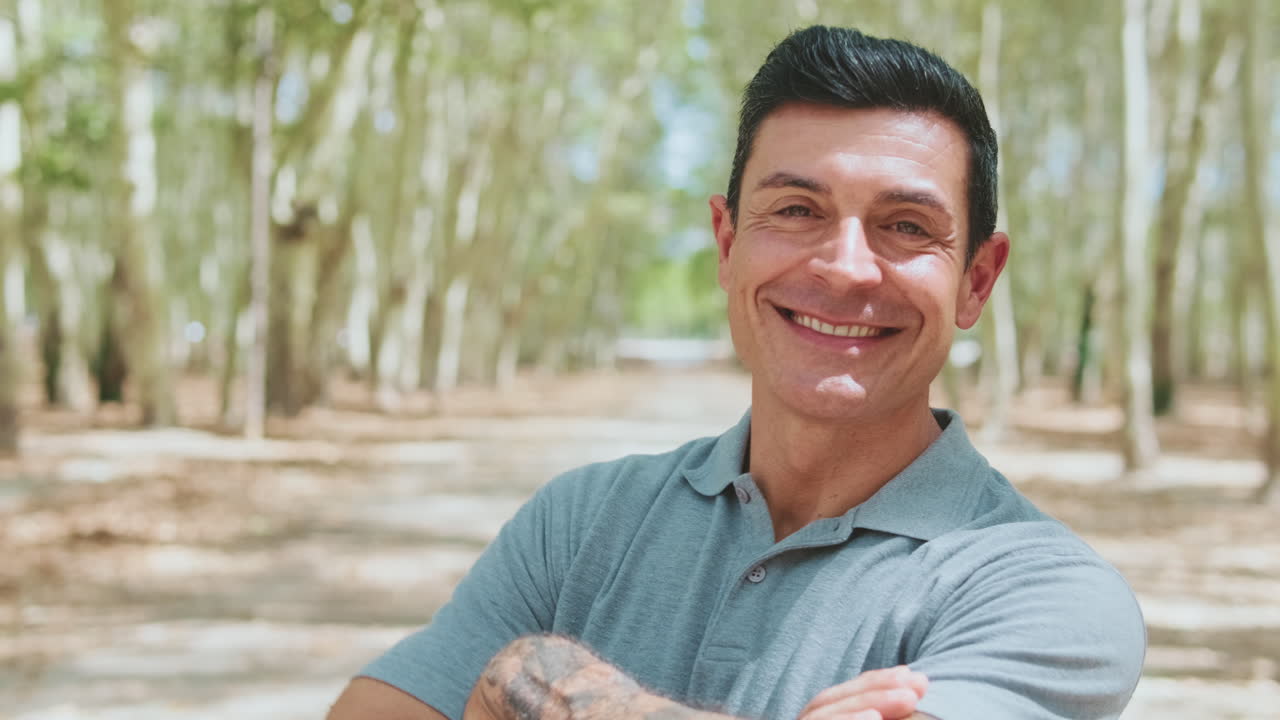 Usmívající se muž se zkříženýma rukama pózuje v parku