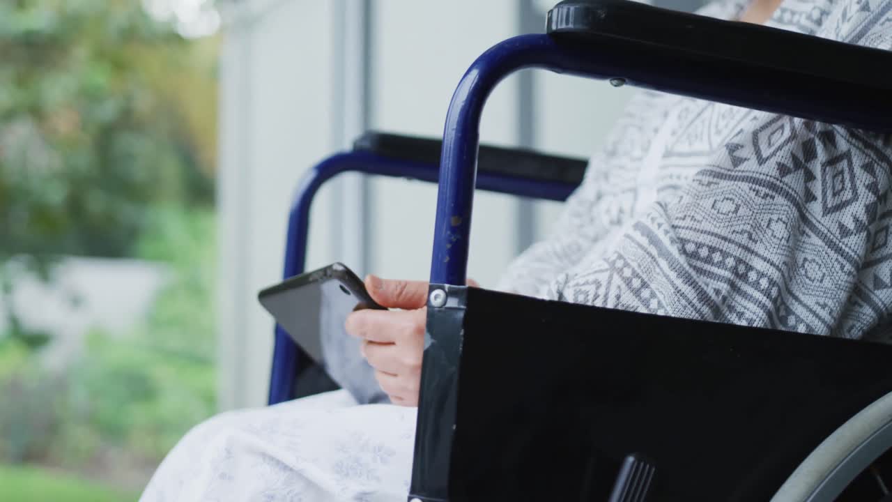Bored asian female patient sitting in wheelchair using smartphone at hospital