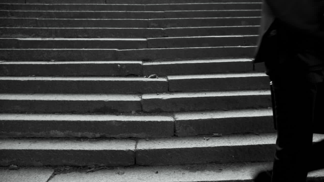 A Man in a Suit with a Skull Mask Sits on Steps