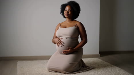 a serene pregnant black woman kneels, gently holding her baby bump