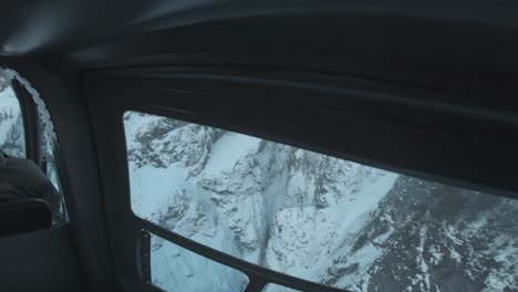 back seat of a helicopter looking at the pilot flying through a mountain range