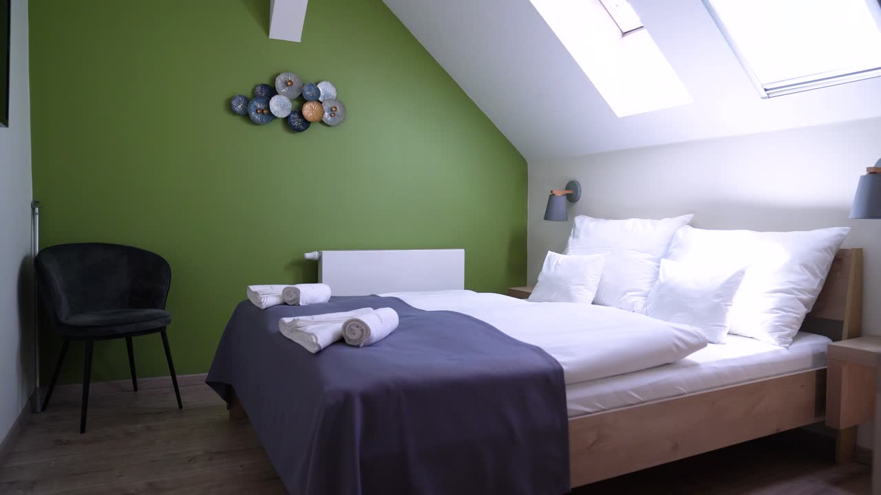 Design d'interni per camera da letto accogliente con parete verde e lucernari, una camera invitante che mostra arredi moderni, un letto confortevole e luce naturale dall'alto.