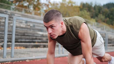 Focused-young-athletic-man-training-on-red-track-of-sports-facility,-tracking-close-up