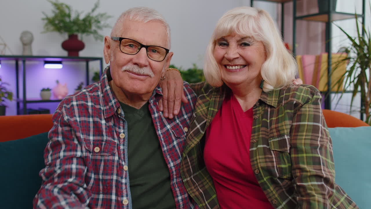 Glad eldre familiepar, besteforeldre, ser inn i kameraet og viser frem nøkler til ny leilighet.