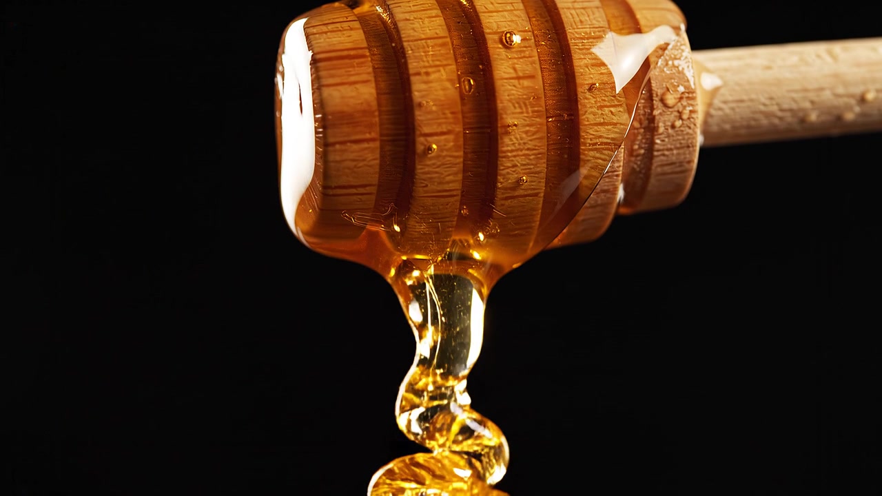 Miele dorato che cola da un mestolo di legno su sfondo nero