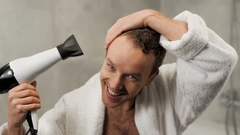 un apuesto hombre rizado se seca el pelo con un secador de pelo en el baño